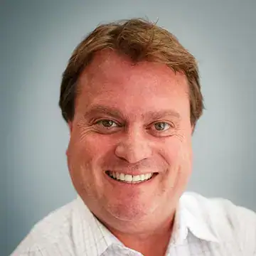 Smiling man with light brown hair wearing a white collared shirt, photographed against a plain light blue background.