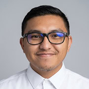 A person with short dark hair, glasses, and a trimmed beard smiles slightly, wearing a white button-up shirt against a plain light background.