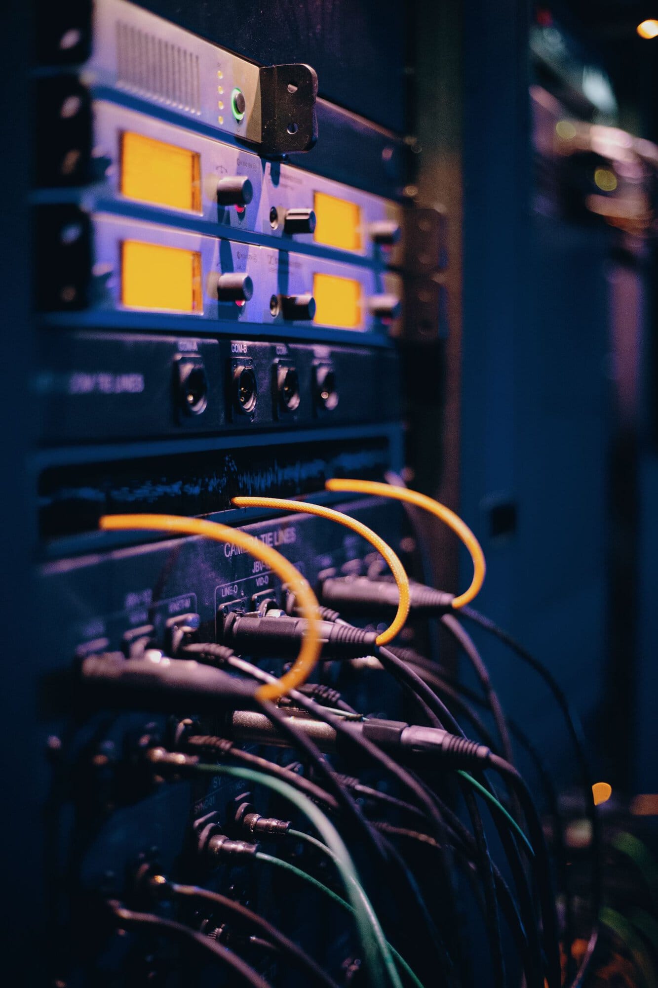 Close-up of a server rack with glowing yellow lights and numerous connected cables in a dimly lit data center environment.