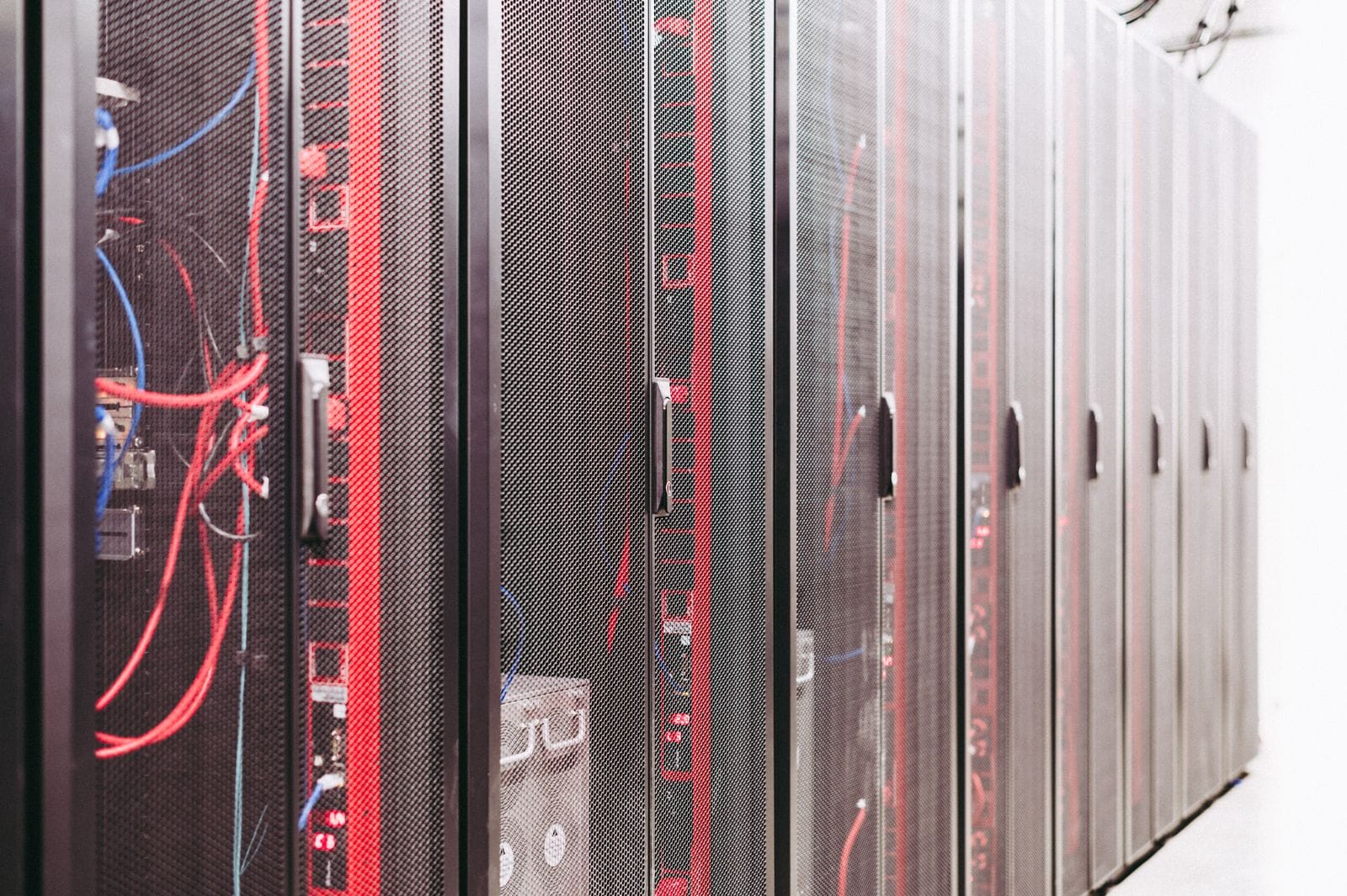 A row of black server racks with visible cables and equipment inside, located in a well-lit data center or server room.